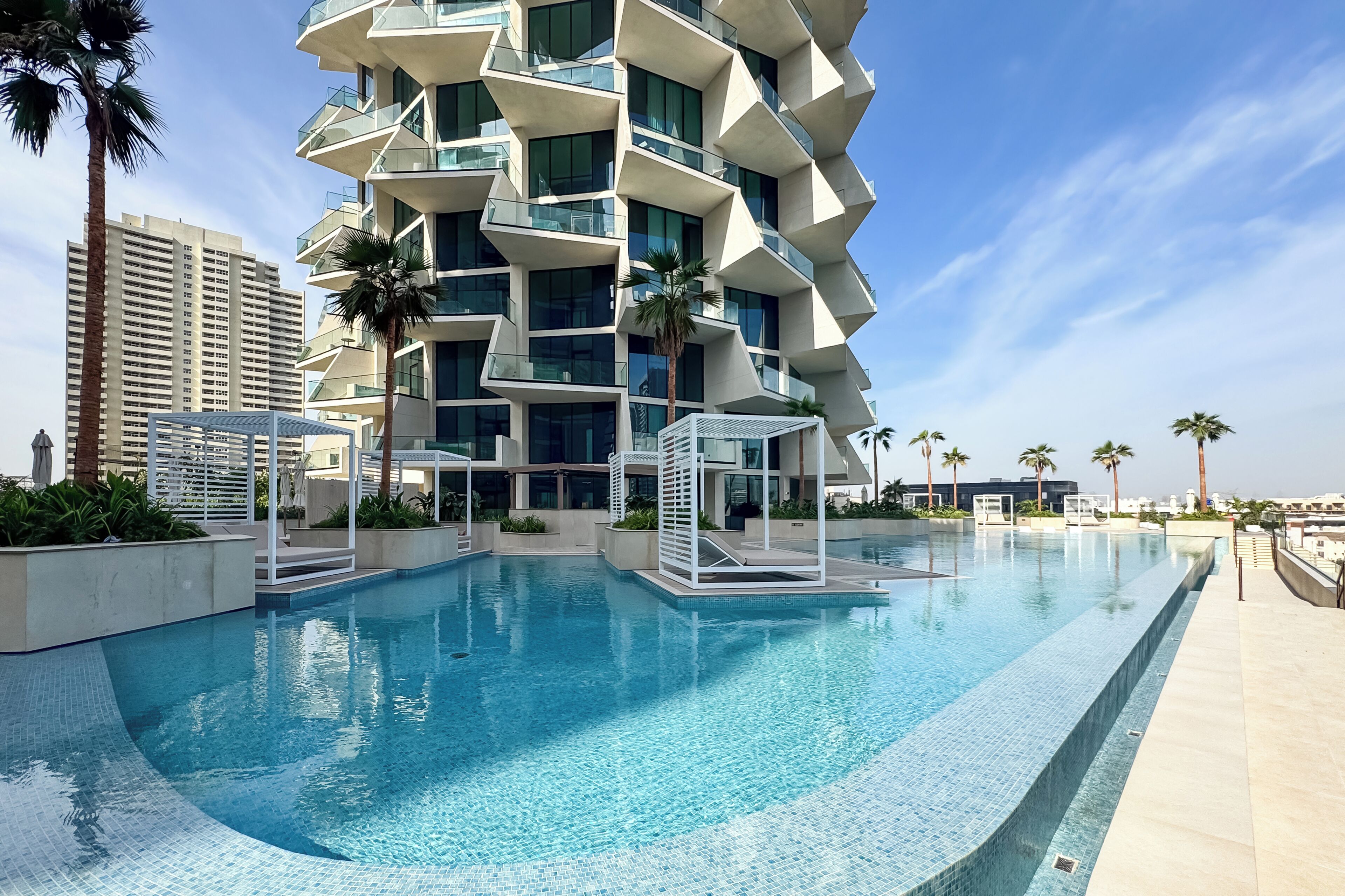 A modern building with a unique zigzag design, a swimming pool, and palm trees.