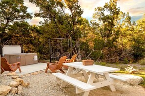 Et udendørs opholdsområde med picnicbord, stole, gyngestativ og et spabad.