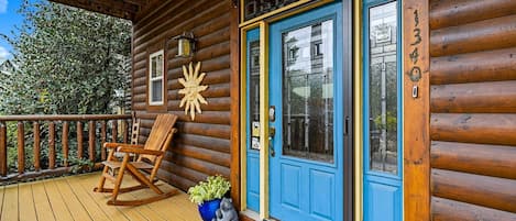 Una cabaña de madera con puerta azul, una mecedora y una pequeña estatua de oso en el porche.
