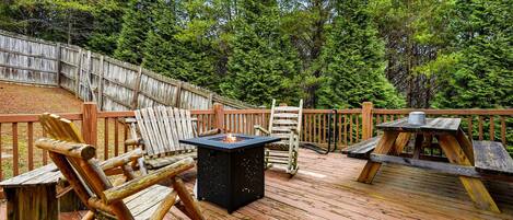 A wooden deck with outdoor furniture, a fire pit, and a wooden fence.