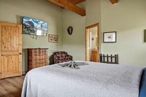 Une chambre à coucher avec un lit, une armoire en bois, une chaise, une commode, un miroir et un tableau accroché au mur.