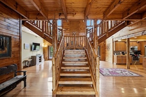 A wooden staircase leading to a second floor, flanked by wooden walls and a kitchen area with modern appliances. - Luxury Log Cabin Escape with Hot Tub, Decks & Family Fun Spaces in Sevierville, Tennessee (Sevierville)