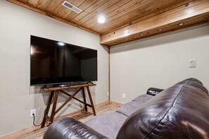 A room with a flat-screen TV on a wooden stand, a leather couch, and a wooden ceiling with recessed lighting. - Luxury Log Cabin Escape with Hot Tub, Decks & Family Fun Spaces in Sevierville, Tennessee (Sevierville)
