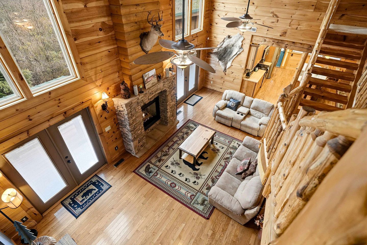 L’intérieur d’une cabane en rondins, avec une cheminée en pierre, un canapé, une table à manger et un ventilateur de plafond.