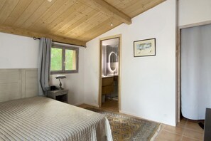 A bedroom with a bed, a nightstand, a window with curtains, a bathroom with a mirror, and a framed picture on the wall. - Holiday Home 'Bergerie Des Estelles' with Mountain View, Wi-Fi and Air Conditioning (Auriol)