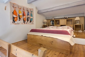A bedroom with a wooden bed, a wall-mounted painting, and built-in wooden shelves with books and decorative items. - Holiday Home 'Bergerie Des Estelles' with Mountain View, Wi-Fi and Air Conditioning (Auriol)