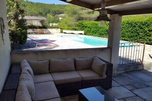 A covered outdoor seating area with a pool, a stone wall, and greenery in the background. - Holiday Home 'Bergerie Des Estelles' with Mountain View, Wi-Fi and Air Conditioning (Auriol)