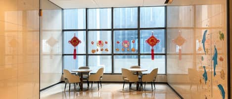 A modern interior with large windows, a dining area with round tables and chairs, and decorative elements on the walls.