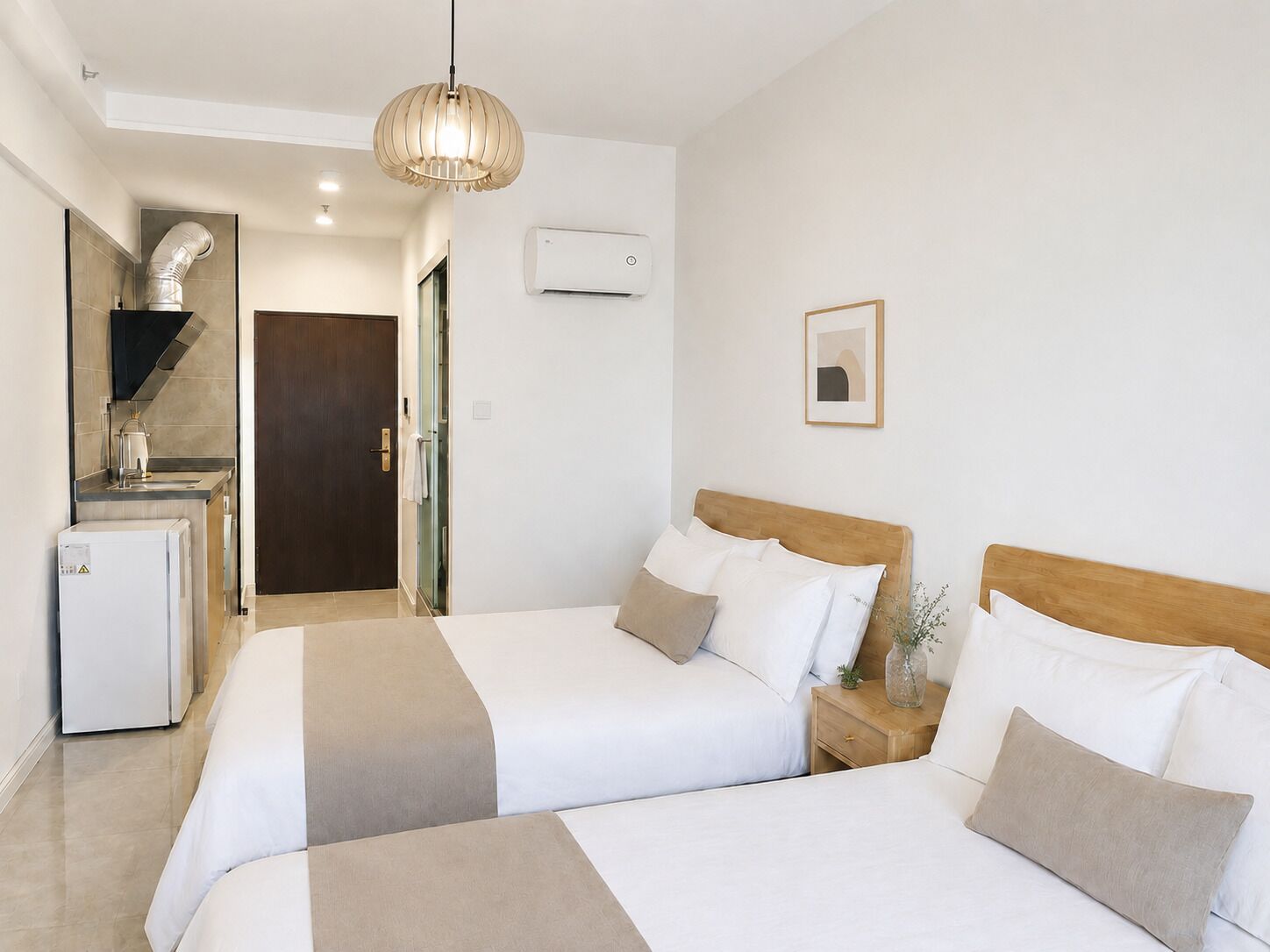 Een hotelkamer met twee bedden, een kitchenette, een houten hoofdeinde, een hanglamp en een lijst met een afbeelding aan de muur.
