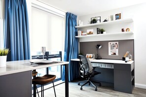 Ein moderner Arbeitsraum mit Schreibtisch, Stuhl, Regalen und einem Fenster mit Vorhängen.