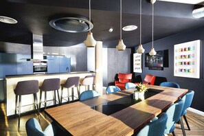 A modern kitchen with a bar area, a dining table with chairs, and a wall with a shelf of canned goods. - Portswood House (Southampton)