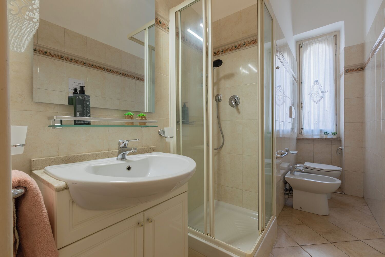 A bathroom with a glass-enclosed shower, a sink, and two toilets.
