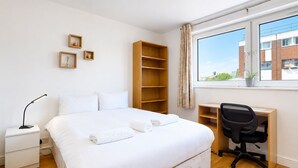 Habitación de hotel moderna con una cama grande, un escritorio, una silla, una mesita de noche y una ventana con vistas a edificios.
