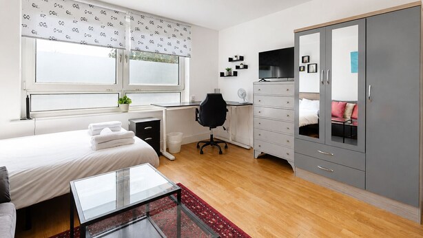 Un dormitorio con cama, escritorio, armario y televisor.