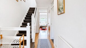 Una escalera conduce a una habitación con baranda blanca, un cuadro en la pared y una ventana con cortinas estampadas.