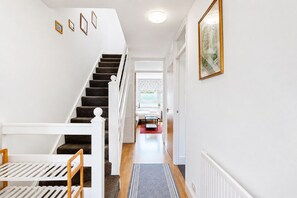 A staircase leading to a room with a white railing, a framed picture on the wall, and a window with patterned curtains. - Bright 3BR-Near Tube-Easy Access to Central London (London)