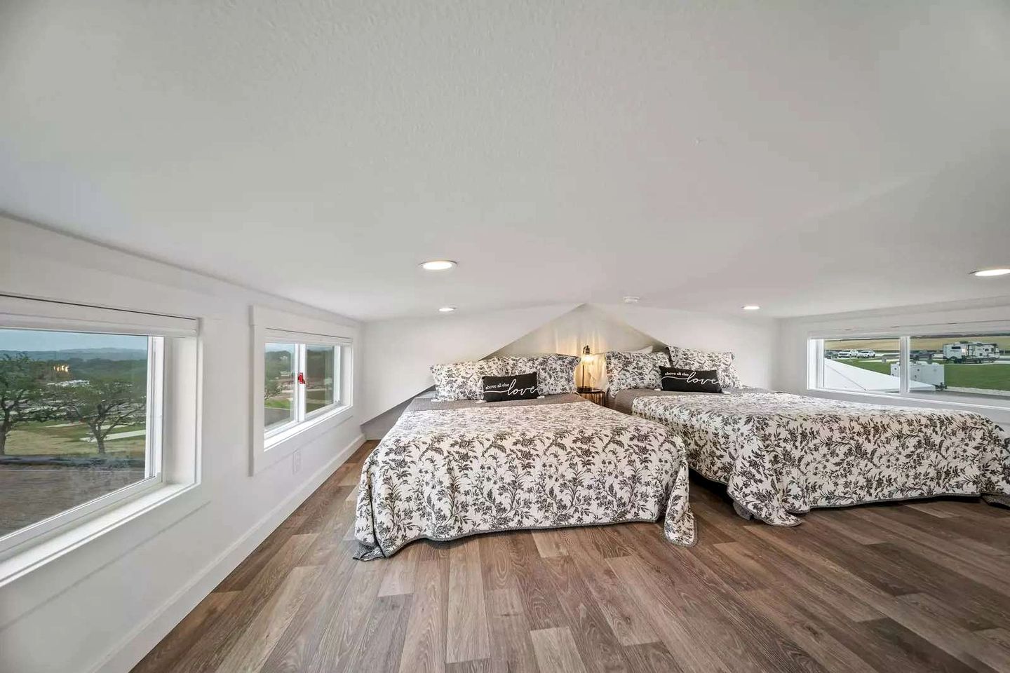 A bedroom with two beds, large windows, and a view of the outside.