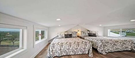 A bedroom with two beds, large windows, and a view of the outside.