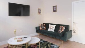 Ein Wohnzimmer mit einer Couch, einem an der Wand befestigten Fernseher, einem kleinen runden Tisch und einem Teppich mit Blumenmuster.