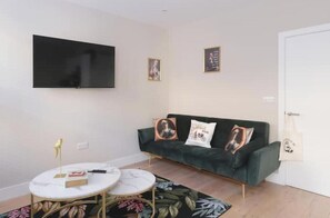 A living room with a sofa, a TV mounted on the wall, a small round table, and a floral rug. - Stylish One-Bedroom Apartment in the Heart of Historic Bath (Bath)