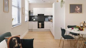Eine moderne Küche mit weißen Schränken, einer schwarzen Arbeitsplatte und einem Essbereich mit weißem Tisch und grünen Stühlen.