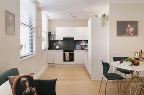 A modern kitchen with white cabinets, a black countertop, and a dining area with a white table and green chairs. - Stylish One-Bedroom Apartment in the Heart of Historic Bath (Bath)
