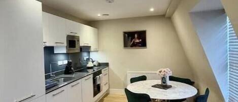 A compact kitchen with modern appliances, a dining table with chairs, and a small window with blinds.