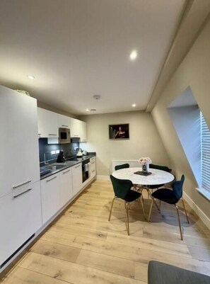 A compact kitchen with modern appliances, a dining table with chairs, and a small window with blinds. - Stylish One-Bedroom Apartment in the Heart of Historic Bath (Bath)