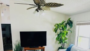 Ein Wohnzimmer mit Deckenventilator, Flachbildfernseher, Couchtisch, Sofa und einer Topfpflanze.