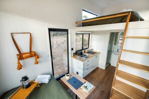 Habitación compacta con literas, kitchenette, escritorio con computadora portátil y una pequeña zona de estar.