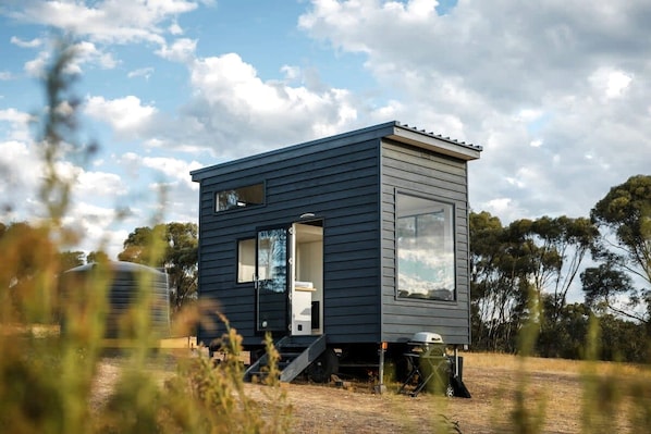 A modern, dark-colored cabin with a small porch, a large window, and a door.
