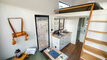A compact room with a bunk bed, a kitchenette, a desk with a laptop, and a small seating area.
