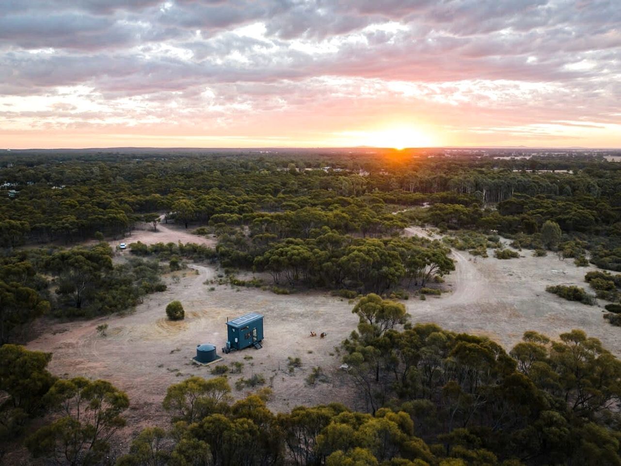 An aerial view of a landscape with scattered trees and a few buildings, including a blue structure.