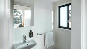 Een badkamer met een witte wastafel, een spiegel, een raam en een handdoekhouder.