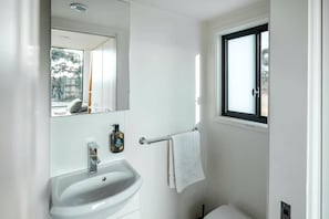Une salle de bain avec un lavabo blanc, un miroir, une fenêtre et un porte-serviettes.