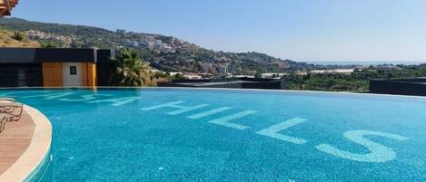 A clear blue infinity pool with 'HILLS' written on the edge, overlooking a hilly landscape.