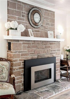 Una chimenea con pared de piedra, un repisa con adornos y un televisor moderno.