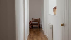 A narrow hallway with wooden flooring, a wooden chair, a radiator, and a door with a knob.