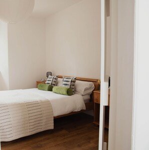A bedroom with a wooden bed, white bedding, and green pillows.