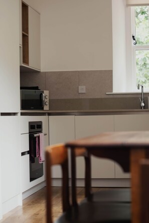Een moderne keuken met witte kastjes, een inbouwoven, een magnetron en een raam boven de gootsteen.