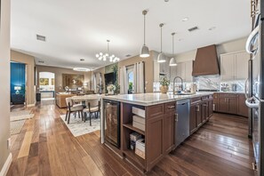 A modern kitchen with wooden flooring, a central island, pendant lighting, and built-in cabinetry.
