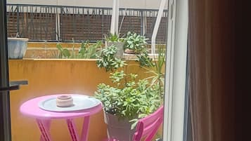 Un balcone con tavolo e sedie, un vaso con una pianta e vista su un edificio sullo sfondo.