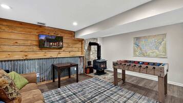 A cozy living room with a wooden wall, a fireplace, a foosball table, and a sofa.
