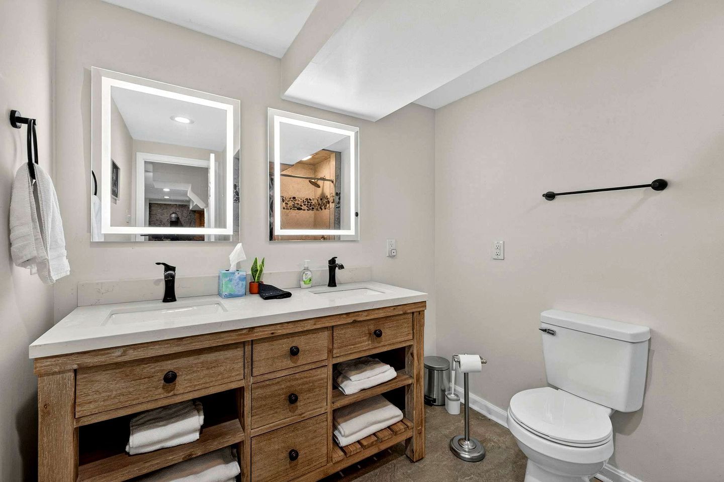 Ein Badezimmer mit einem Holzkonsolenunterschrank, zwei Spiegeln, einer Toilette und einem Handtuchhalter.