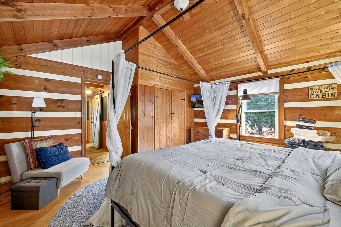 A cabin interior with a large bed, a sofa, a desk, and a window with a view.