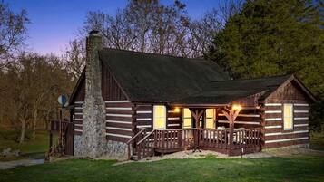 A log cabin with a stone chimney, wooden porch, and a small deck.