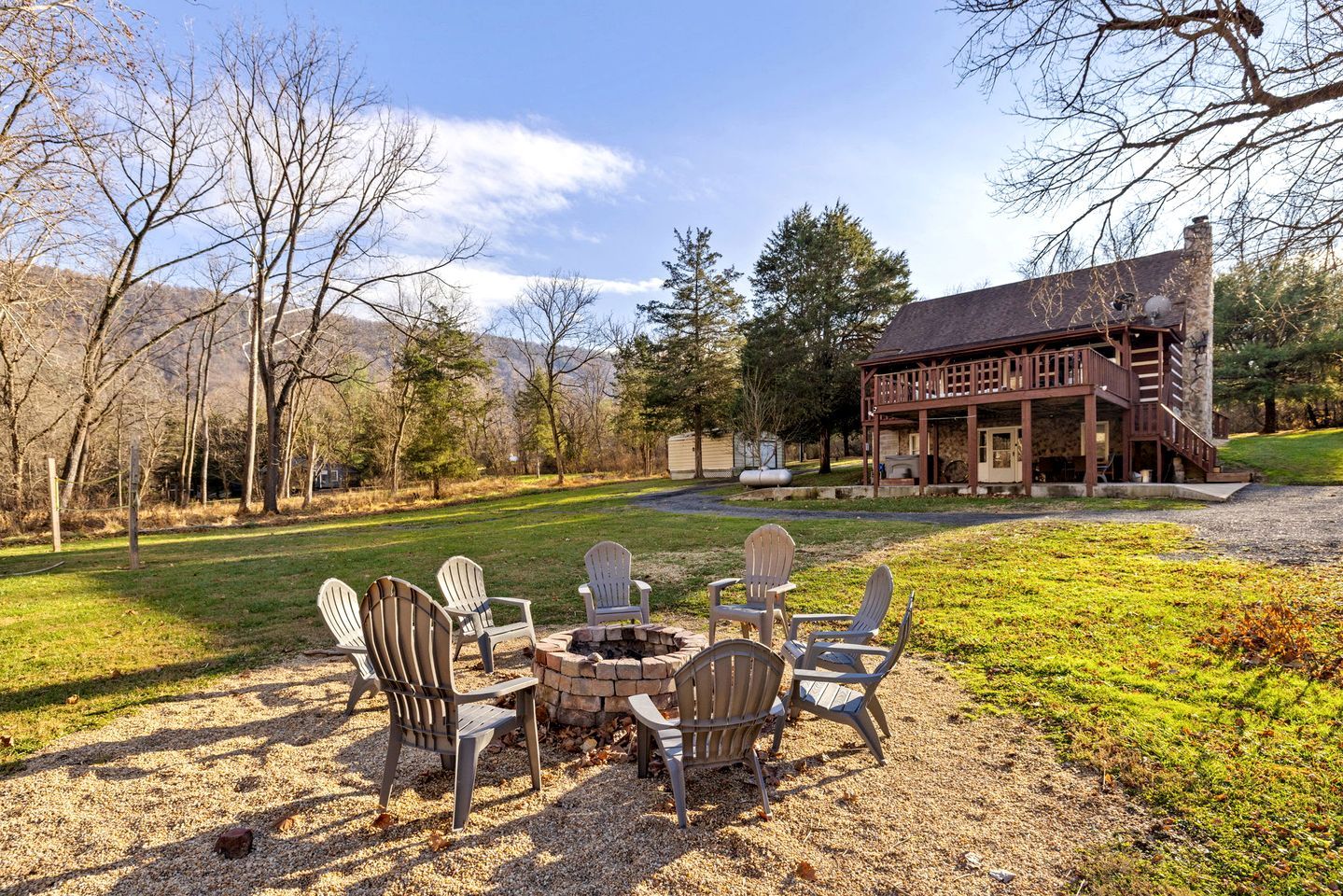 A lodge with a stone fireplace and Adirondack chairs in the yard.