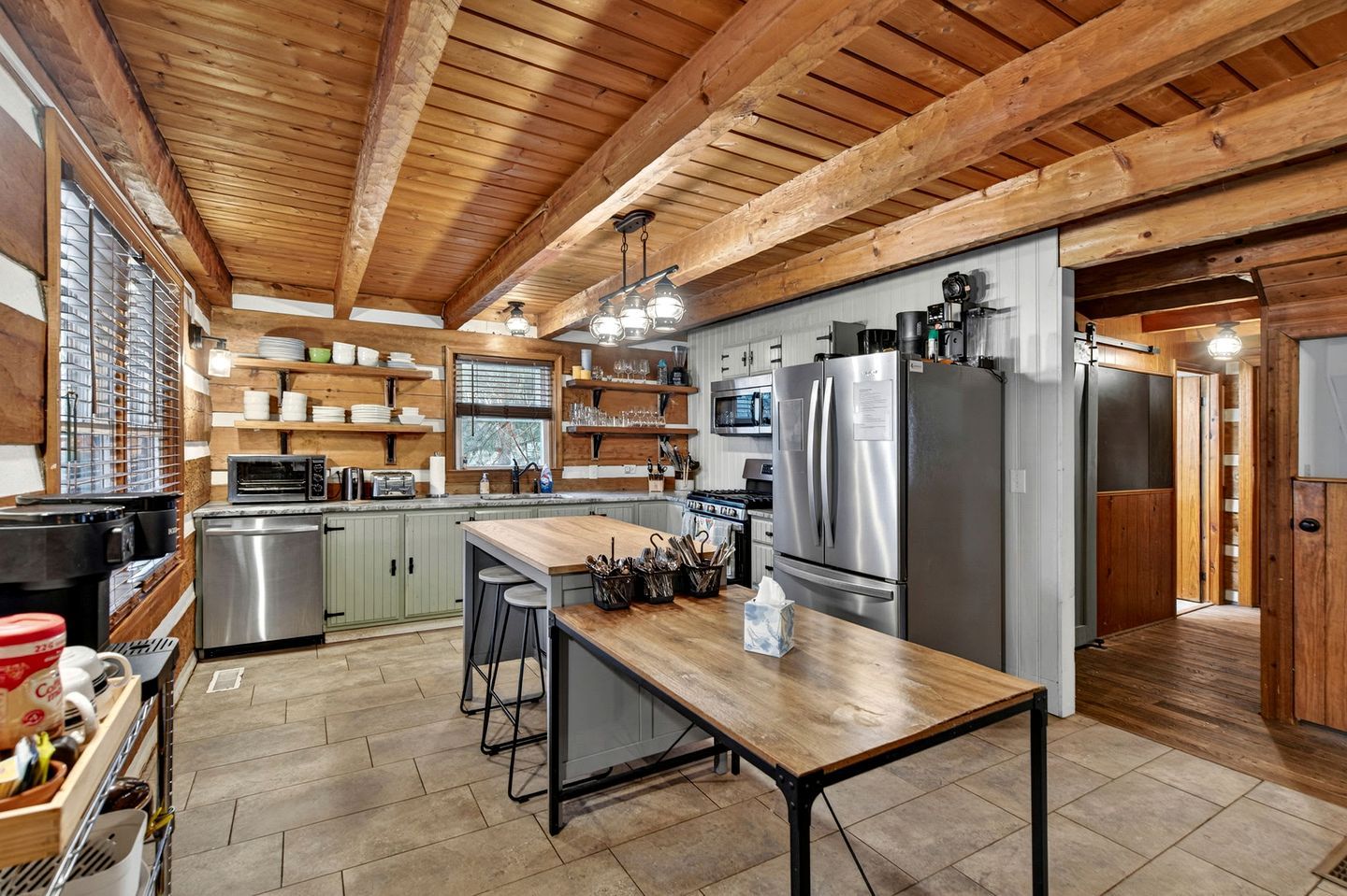 A spacious kitchen with wooden beams, stainless steel appliances, and a central island with stools.