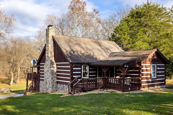 Une cabane en rondins avec une cheminée en pierre, une terrasse en bois et un porche doté de balustrades.