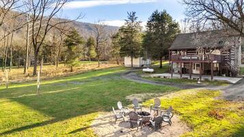 A lodge with a fire pit and outdoor seating, surrounded by a grassy yard and trees.
